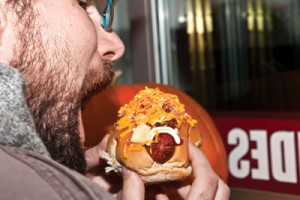 Photo by Rachel Frey. Mike Mckiel prepares to sink his teeth into an A-bomb, a hot dog topped with mustard, mayo, ketchup, bacon, cheese and BBQ potato chips which can be found at Tubby Dog.