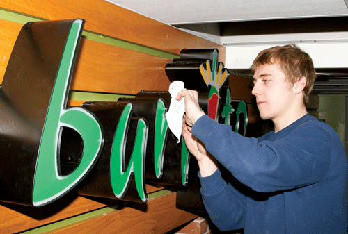 Photo by Jorden Dixon. Dylan Brown, of Topmade Plastics and Neon Signs Ltd., puts some finishing touches on the Mucho Burrito sign.