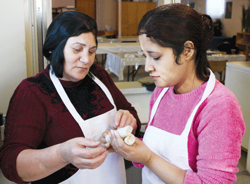 Photo by Asha Siad.  Victoria Jiddoo, left, instructs Jyoti Sharma on how to delicately wrap a vegetable spring roll. EthniCity catering, a social enterprise of the Centre for Newcomers, gives these women the opportunity to gain Canadian work experience. 